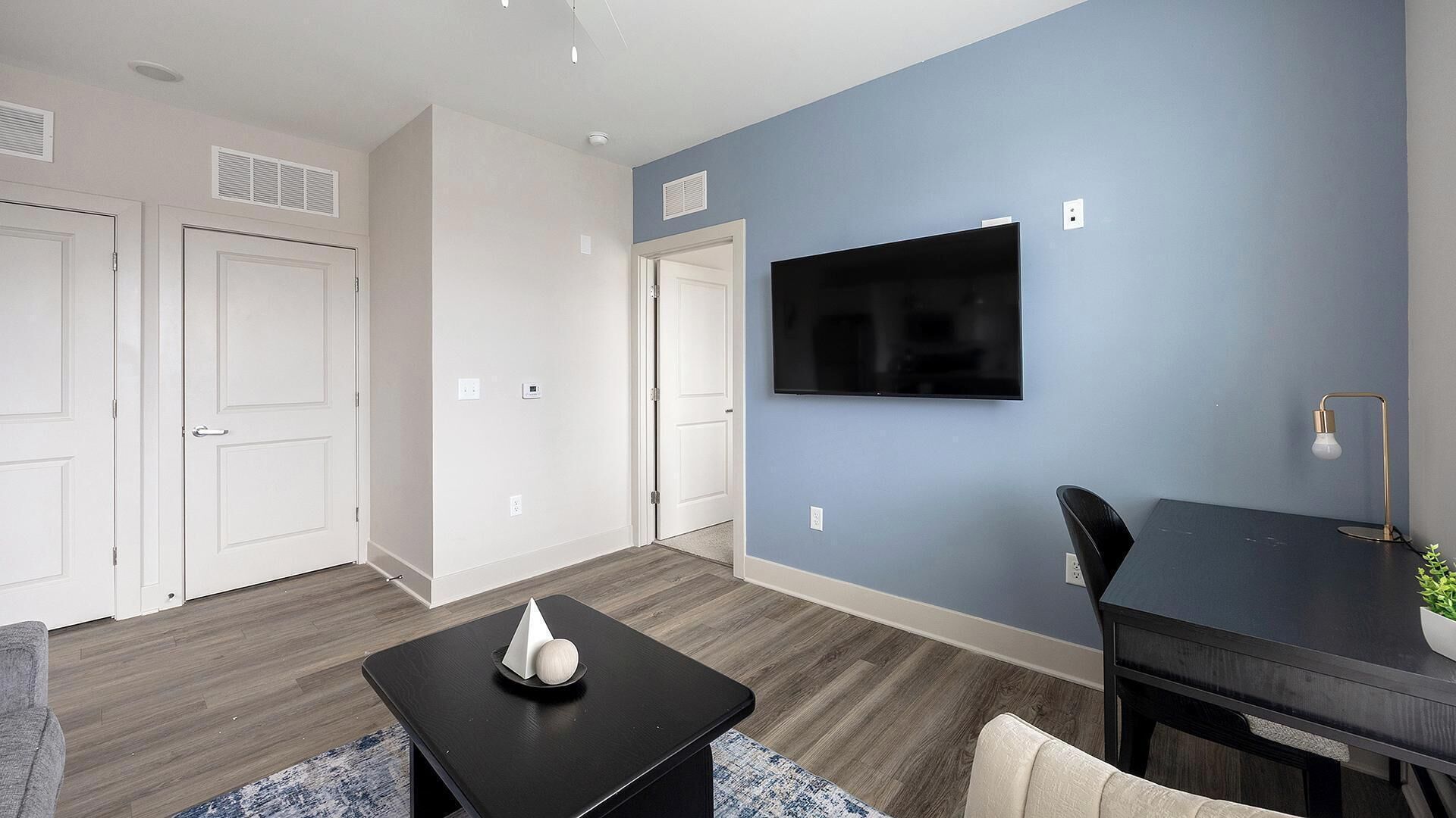 A modern living room with a flat-screen TV, a dark wooden coffee table, and a dining area with a table and chairs.