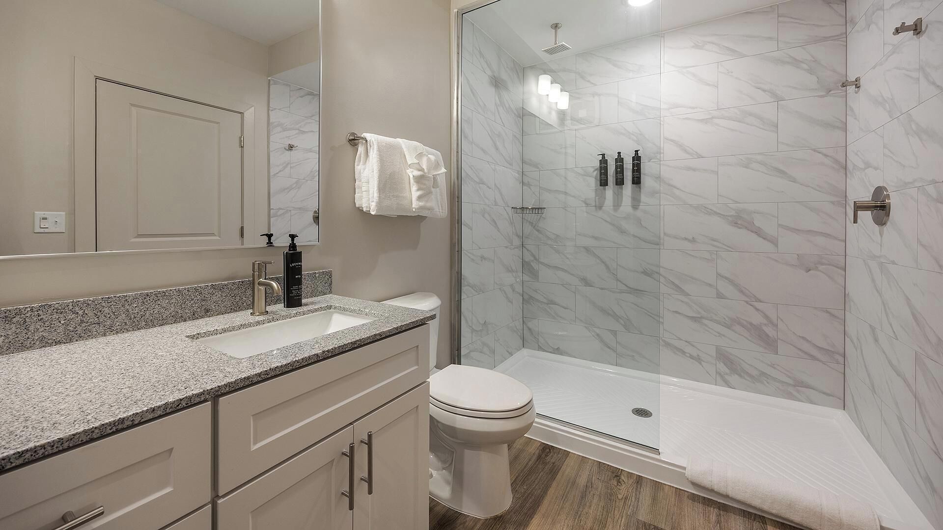 A modern bathroom with a glass-enclosed shower, a sink with a marble countertop, and a toilet.