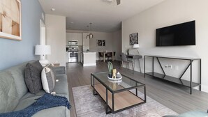 A modern living room with a sofa, coffee table, and a TV. - Landing | Modern 2BD, Gym (Saint Johns)