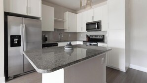 A modern kitchen with white cabinetry, a stainless steel refrigerator, a microwave, a stove, and a water dispenser. - Landing | Modern 2BD, Gym (Saint Johns)