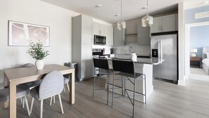 Een moderne keuken met een eethoek, met een centraal keukenblok, barkrukken en een hangende lamp.