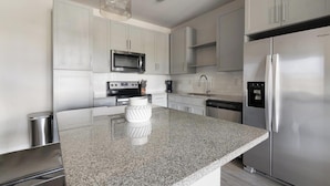 Een moderne keuken met roestvrijstalen apparatuur, witte kastjes en een granieten aanrecht.