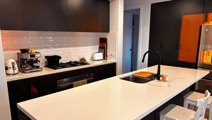Une cuisine moderne avec des meubles de couleur sombre, un plan de travail blanc, une machine à café, un grille-pain et un réfrigérateur.