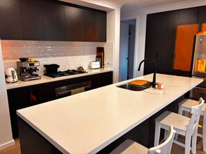 A modern kitchen with dark cabinets, a white countertop, a coffee machine, a toaster, and a refrigerator.