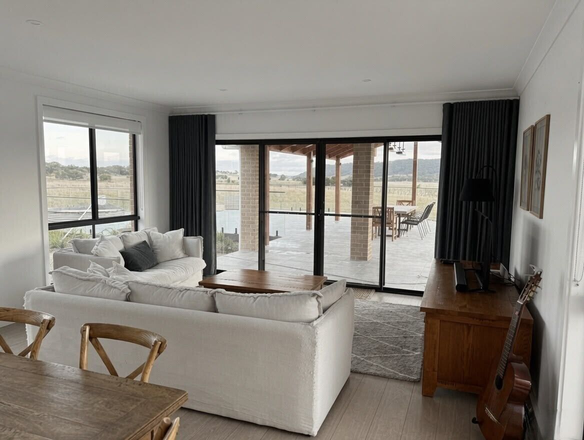 A modern living room with a sofa, dining table, and chairs. There is a large window with a view of the outdoors.