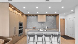 Una cocina moderna con electrodomésticos integrados, una isla central con taburetes de bar y un comedor de madera.