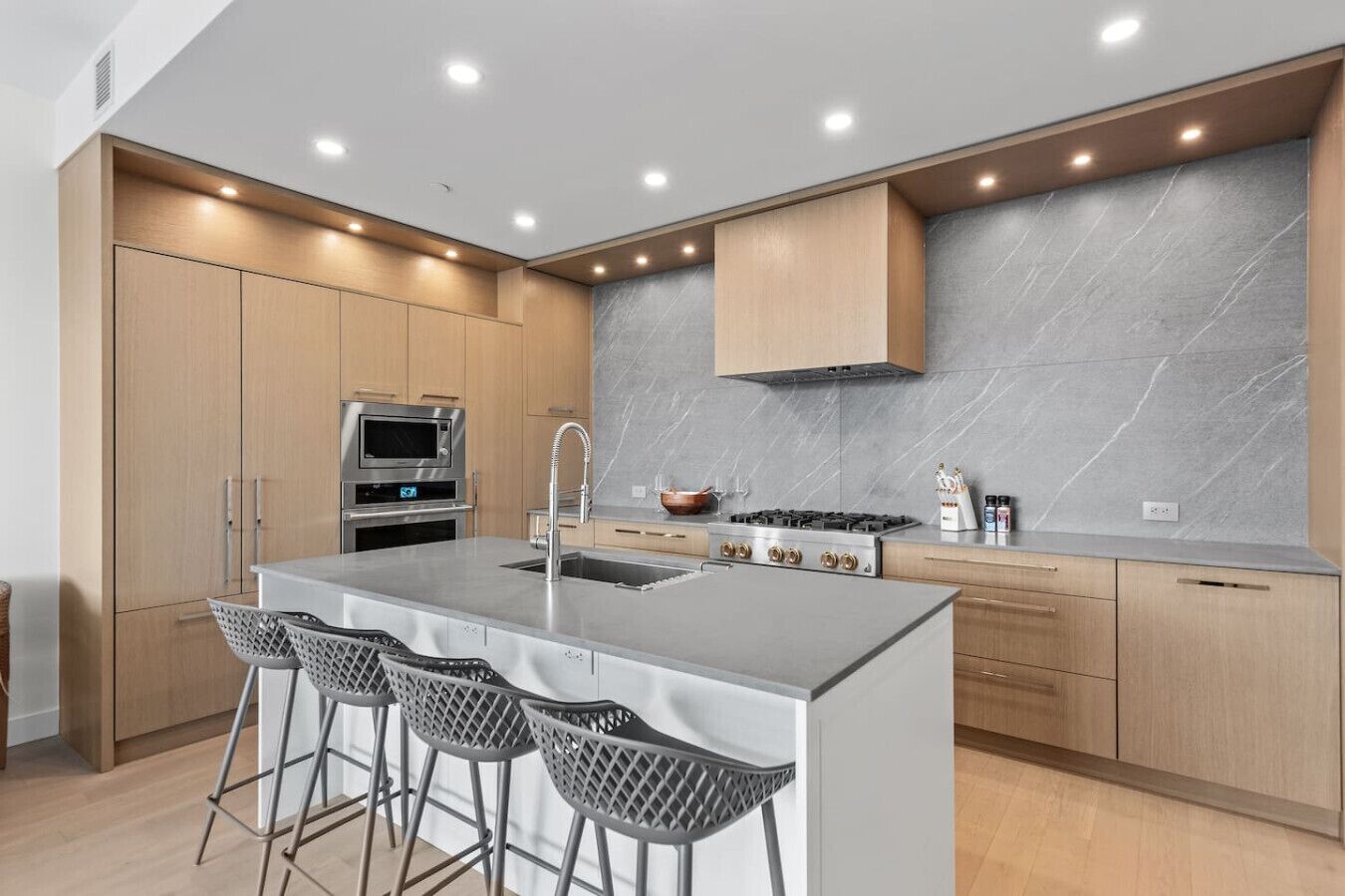 Una cocina moderna con una isla, taburetes de bar, horno empotrado y estufa.