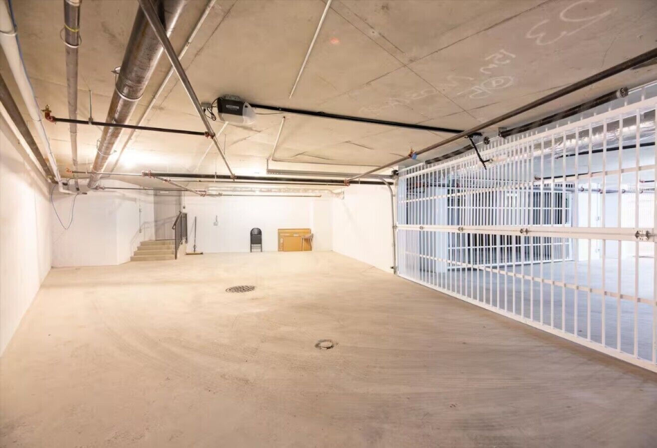Ruime parkeergarage met betonnen vloeren, een trap en een wit metalen hek.