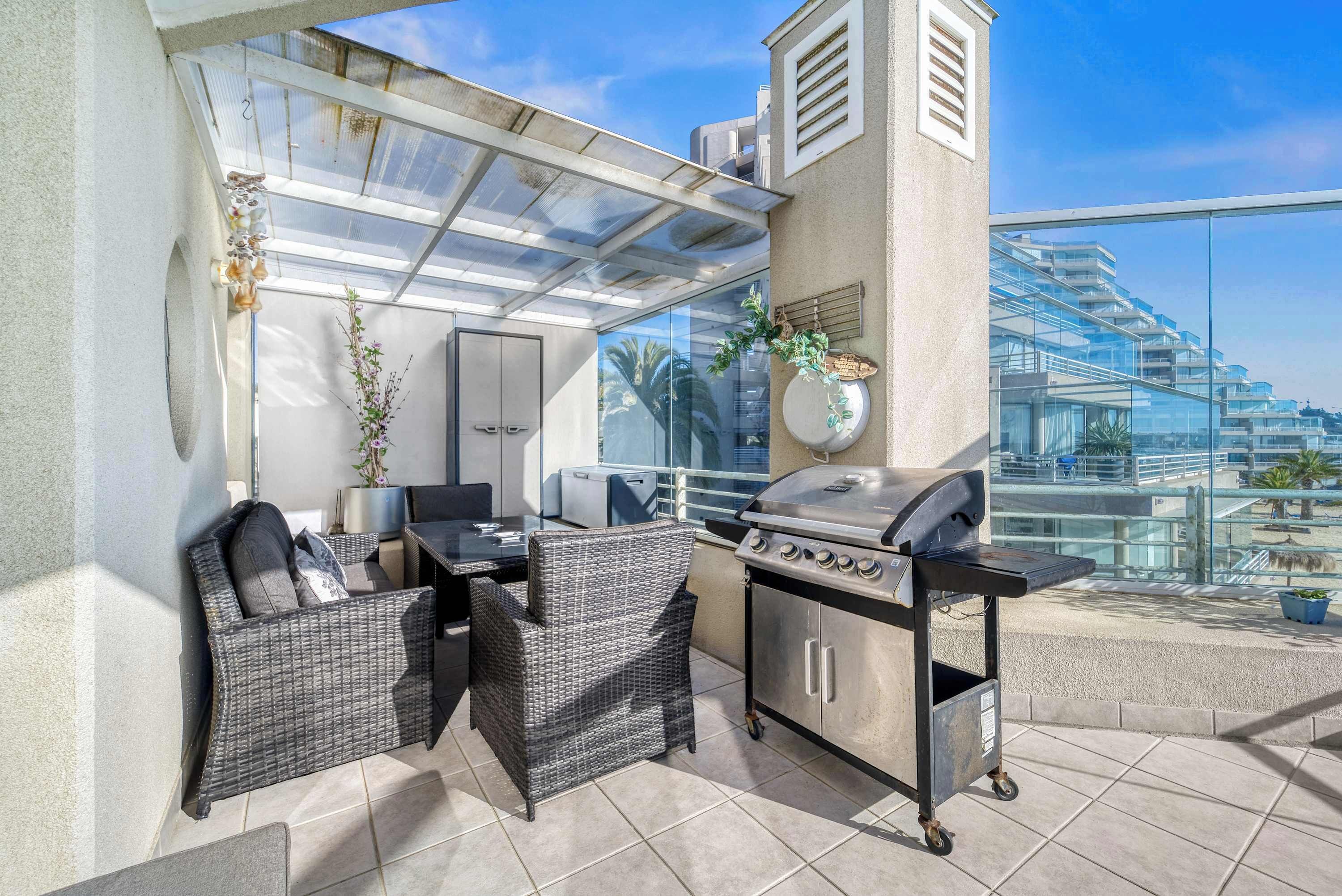 Un patio exterior con una parrilla, mobiliario de mimbre y vistas a un edificio moderno.