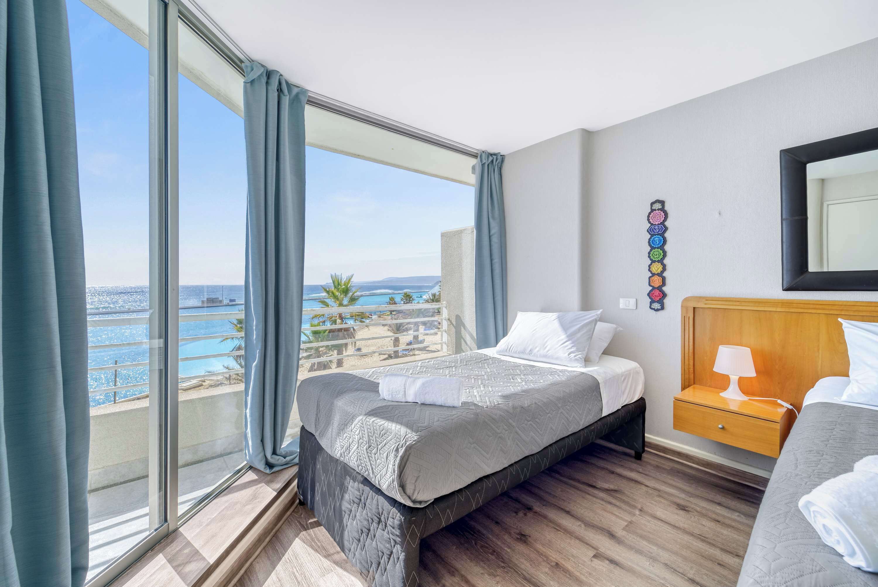 A hotel room with a large window, a bed, a bedside table, and a view of the sea.