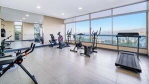 Un gimnasio con diferentes equipos de ejercicio, ventanas amplias y vistas al exterior.