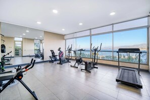 Un gimnasio con diferentes equipos de ejercicio, ventanas amplias y vistas al exterior.