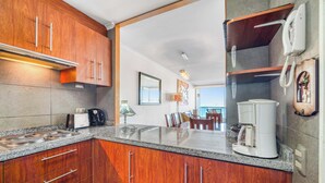 Una cocina moderna con encimeras de granito, armarios de madera, estufa integrada y cafetera.