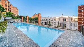 Una piscina en la azotea con un cielo azul despejado, rodeada de edificios con fachadas de ladrillo y blanco.