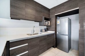 Eine moderne Küche mit dunklen Holzausführungen, einem Edelstahlkühlschrank und einer eingebauten Mikrowelle.