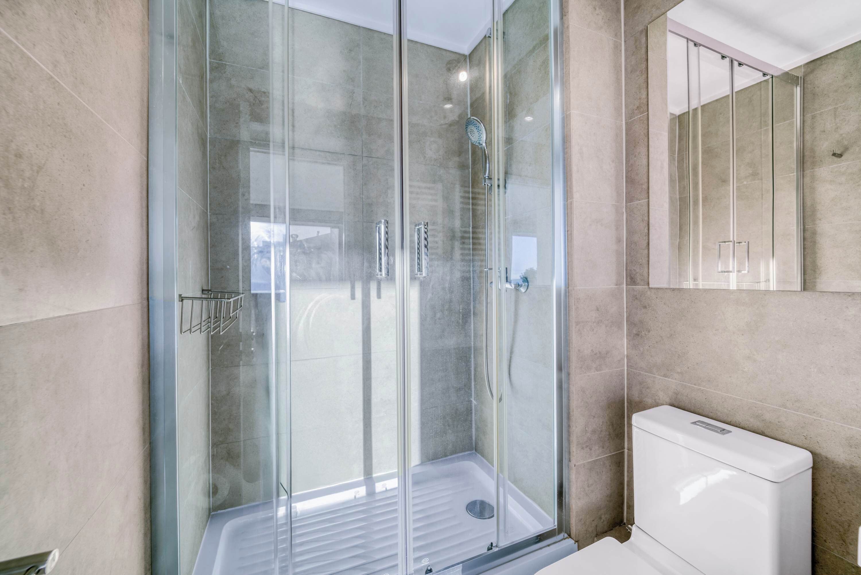 Ein modernes Badezimmer mit einer gläsernen Dusche, einer weißen Toilette und einem großen Spiegel.