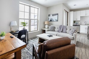 A modern living room with a sofa, coffee table, and a dining area with a wooden table and chairs. - Landing | Stylish 1BD, Courtyard, Gym (Cleveland)
