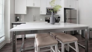 Una cocina moderna con armarios blancos, un refrigerador de acero inoxidable, un microondas y un florero con una planta en la isla.