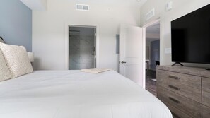 Un dormitorio con cama, cómoda, televisor y puerta de baño.