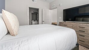 Un dormitorio con cama, televisión, armario y baño visible a través de una puerta abierta.