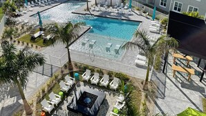 Zona de piscina en la azotea con sillas de descanso y bañera de hidromasaje, rodeada de palmeras y un complejo de edificios.