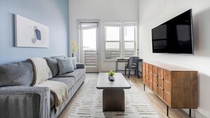Un salon moderne avec un canapé gris, une table basse en bois, un téléviseur fixé au mur et une grande fenêtre donnant sur un beau paysage.