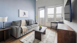 Un salon moderne avec un canapé gris, une table basse en bois, un bureau et une grande fenêtre donnant sur un beau paysage.