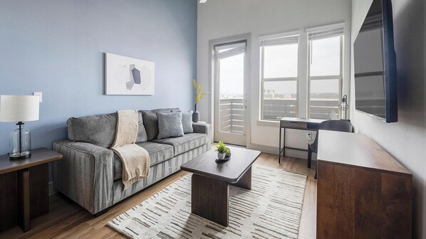 Ein modernes Wohnzimmer mit grauem Sofa, einem Holztisch, einem Schreibtisch und einem großen Fenster mit Blick.