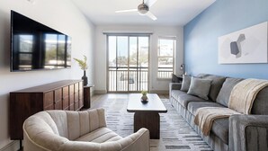 Uma sala de estar com sofá, poltrona, televisão e ventilador de teto.