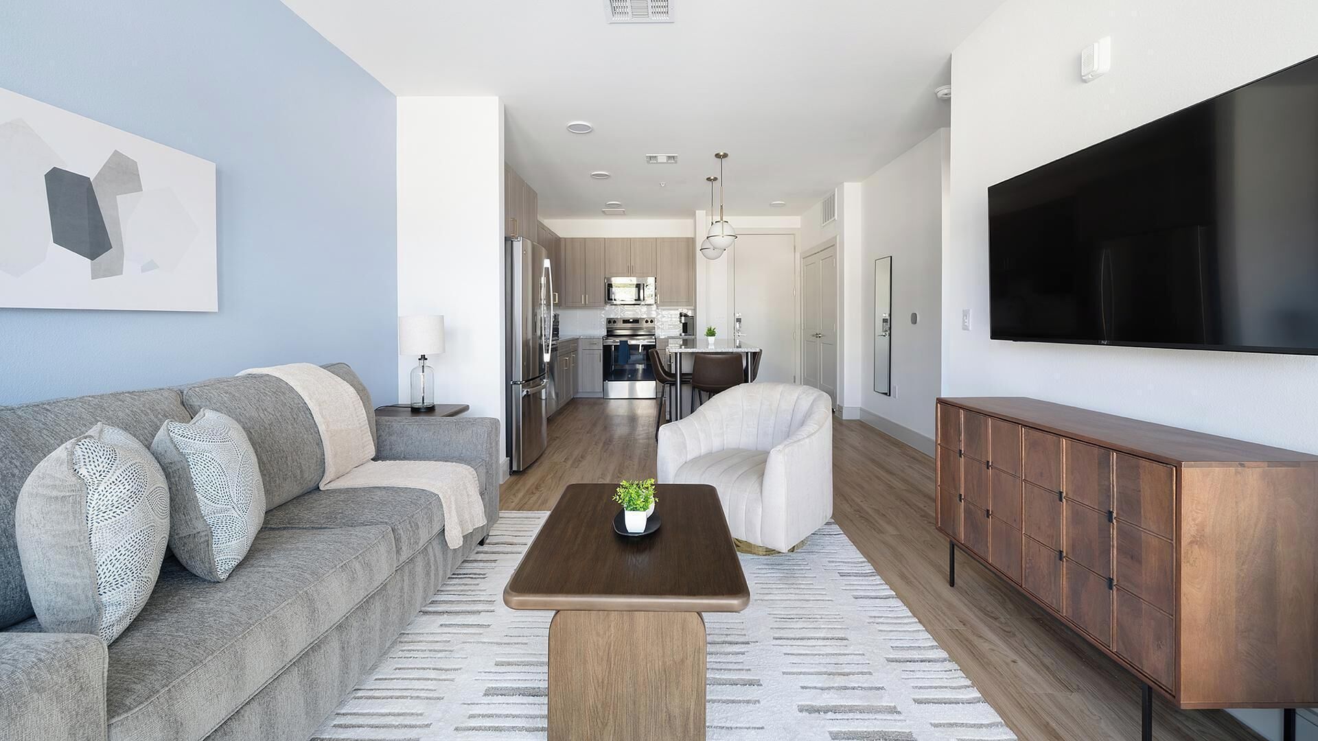 A modern living room with a sofa, a coffee table, a TV, and a kitchen in the background.