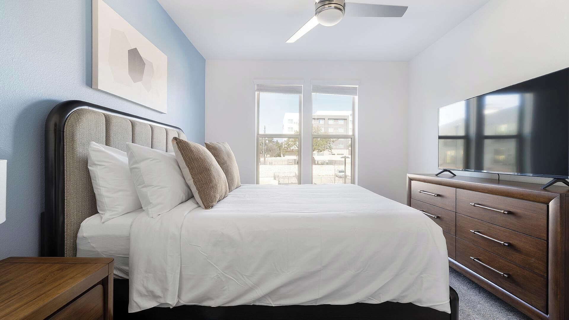 A bedroom with a bed, a dresser, a TV, and a ceiling fan.