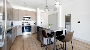 Uma cozinha moderna com eletrodomésticos de aço inoxidável, piso de madeira e um espaço bar com banquetas.