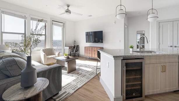 Una cocina moderna con una isla central, un comedor con sofá y mesa de centro, y una sala de estar con televisor.