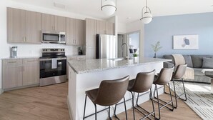 Una cocina moderna con una isla central, taburetes de bar, electrodomésticos de acero inoxidable y una pared de color azul claro.