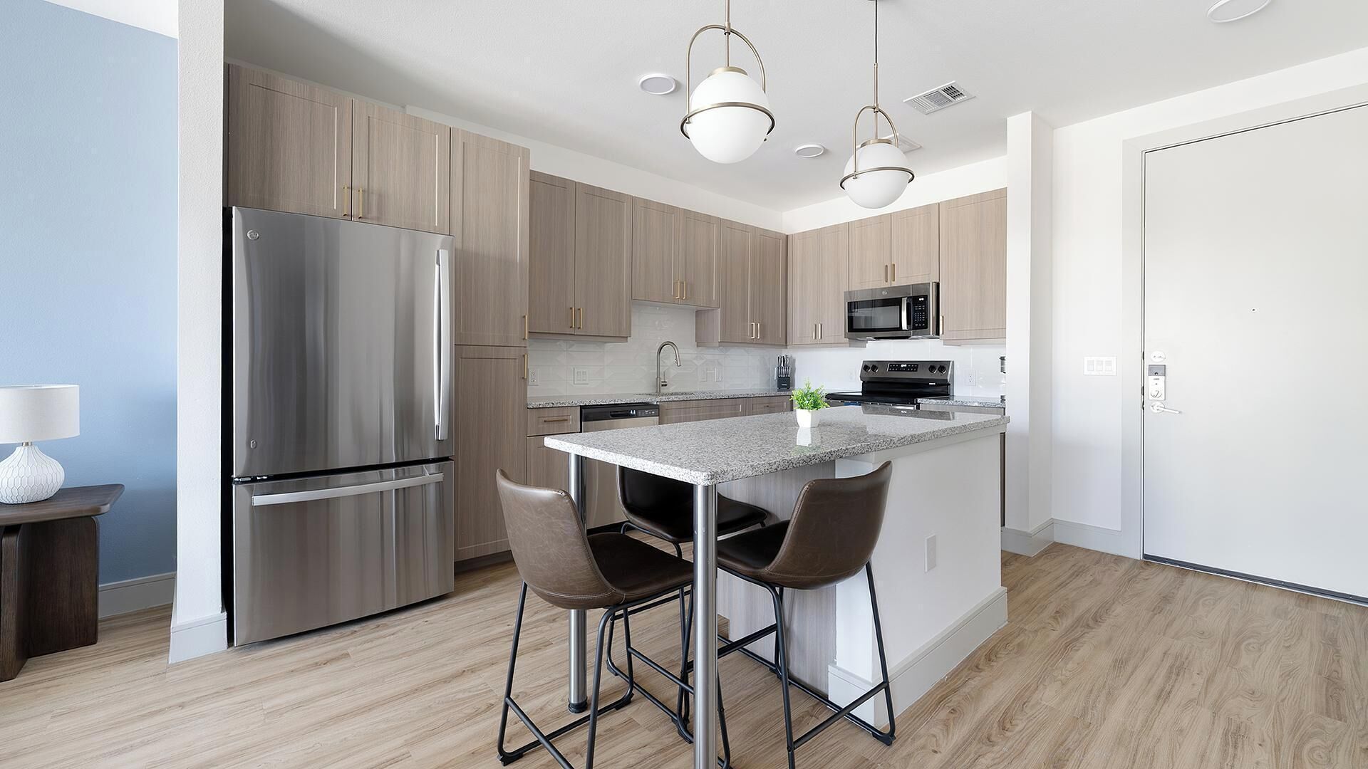 Een moderne keuken met roestvrijstalen apparatuur, een centraal kookeiland met barkrukken en licht houten kastjes.