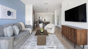 A modern living room with a sofa, coffee table, TV, and a dining area. - Landing | Spectacular 1BD, Clubhouse, Pool (Austin)