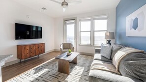 A living room with a flat-screen TV, a wooden cabinet, a grey sofa, a patterned rug, and a ceiling fan. - Landing | Modern 2BD, Pool, Clubhouse (Austin)