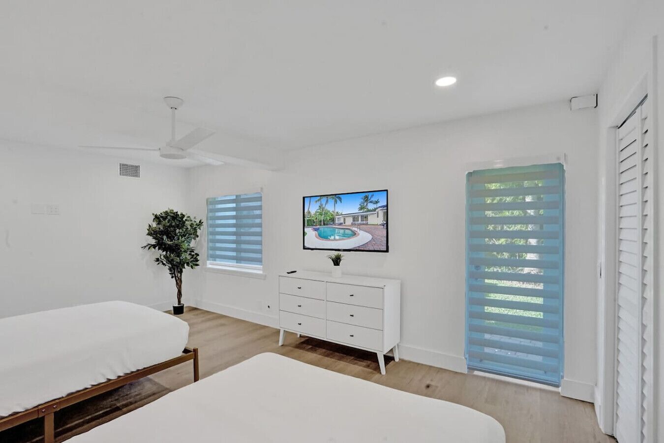 A bedroom with two beds, a dresser, a TV, and a window with blinds.