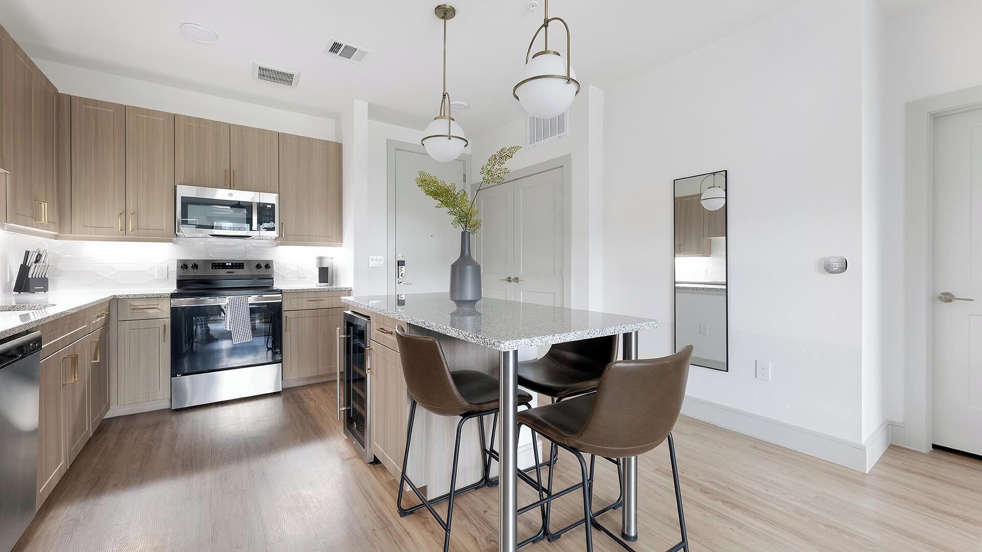 A modern kitchen with stainless steel appliances, a marble countertop, and a central island with bar stools.