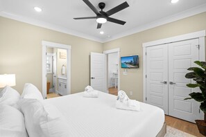 Una habitación de hotel con cama, ventilador de techo, televisión y puertas blancas.