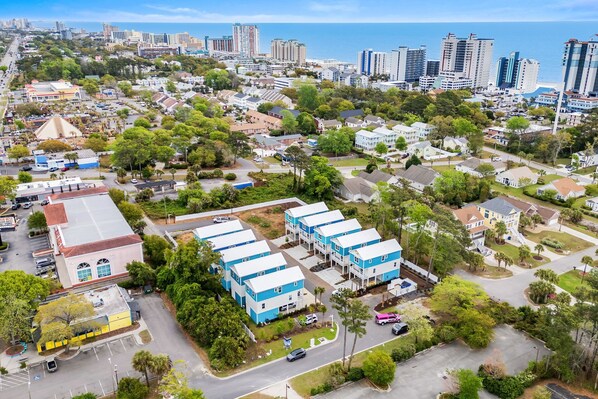 Vista aérea de una zona residencial con casas unifamiliares y edificios de apartamentos, rodeada de vegetación y un paisaje costero al fondo.