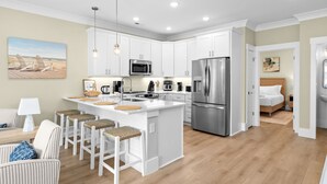 Una cocina moderna con armarios blancos, electrodomésticos de acero inoxidable y una isla central con taburetes de bar.