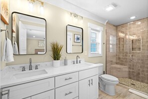 Un baño con tocador blanco, un espejo grande, inodoro y cabina de ducha con mampara de vidrio.