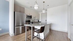 A modern kitchen with stainless steel appliances, a granite countertop, and a bar stool. - Landing | Beautiful 1BD, Pool, Clubhouse (Austin)
