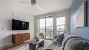 Un salon équipé d’un téléviseur à écran plat, d’un meuble en bois, d’un canapé gris et d’un ventilateur de plafond.