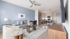 A modern living room with a sofa, coffee table, and a dining area with bar stools. - Landing | Amazing 1BD, Clubhouse, Pool (Austin)