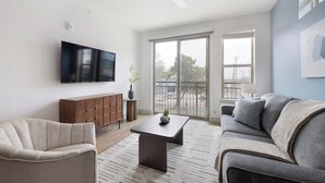 A modern living room with a flat-screen TV, a wooden cabinet, a grey sofa, and a coffee table. - Landing | Stunning 1BD, Clubhouse, Gym (Austin)