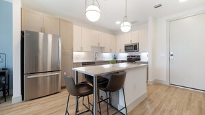 A modern kitchen with stainless steel appliances, a central island with bar stools, and pendant lighting. - Landing | Stunning 1BD, Clubhouse, Gym (Austin)