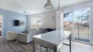 Uma cozinha moderna com bancada de granito, área de refeições com mesa e cadeiras, sofá cinza e ventilador de teto.