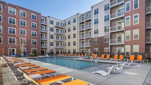 A multi-story residential building with a swimming pool, outdoor seating, and balconies. - Landing | Incredible 1BD, Gym, Game Room (Richmond)